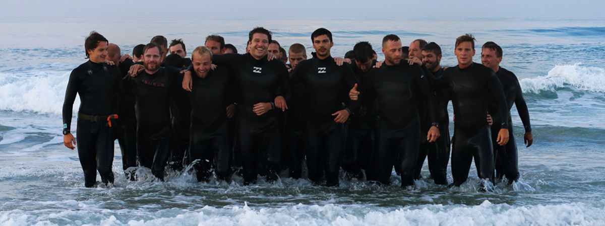 Group of men in wetsuits standing in the ocean after surf passage