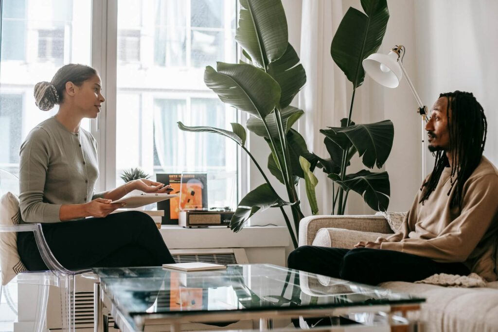 A therapist in a gray sweater is talking to a man sitting on a couch about Xanax addiction treatment options.