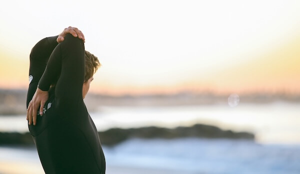 A man in a black wetsuit stretching next to the ocean while attending a rehab in California.